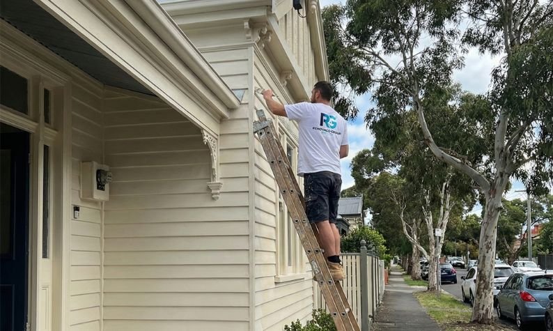 Renovaco painter on a ladder preparing and painting weatherboard on a Melbourne home